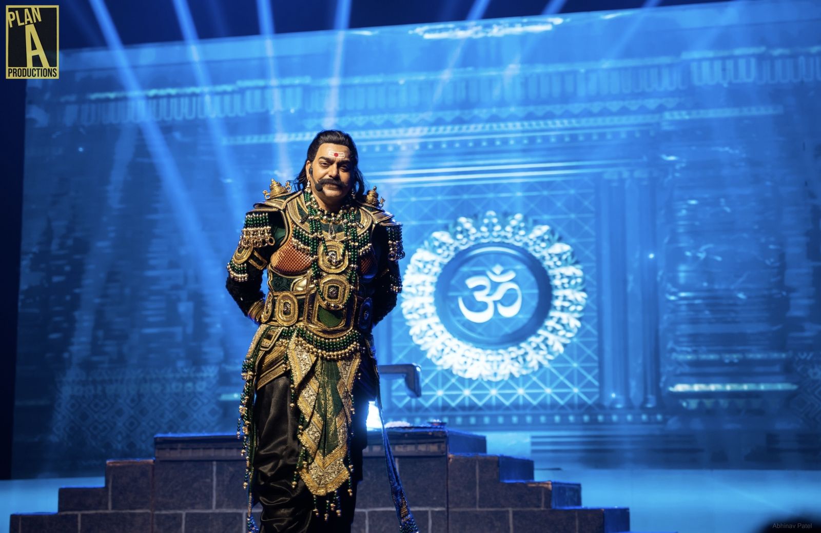 Actor in a green and gold costume on a blue-lit stage
