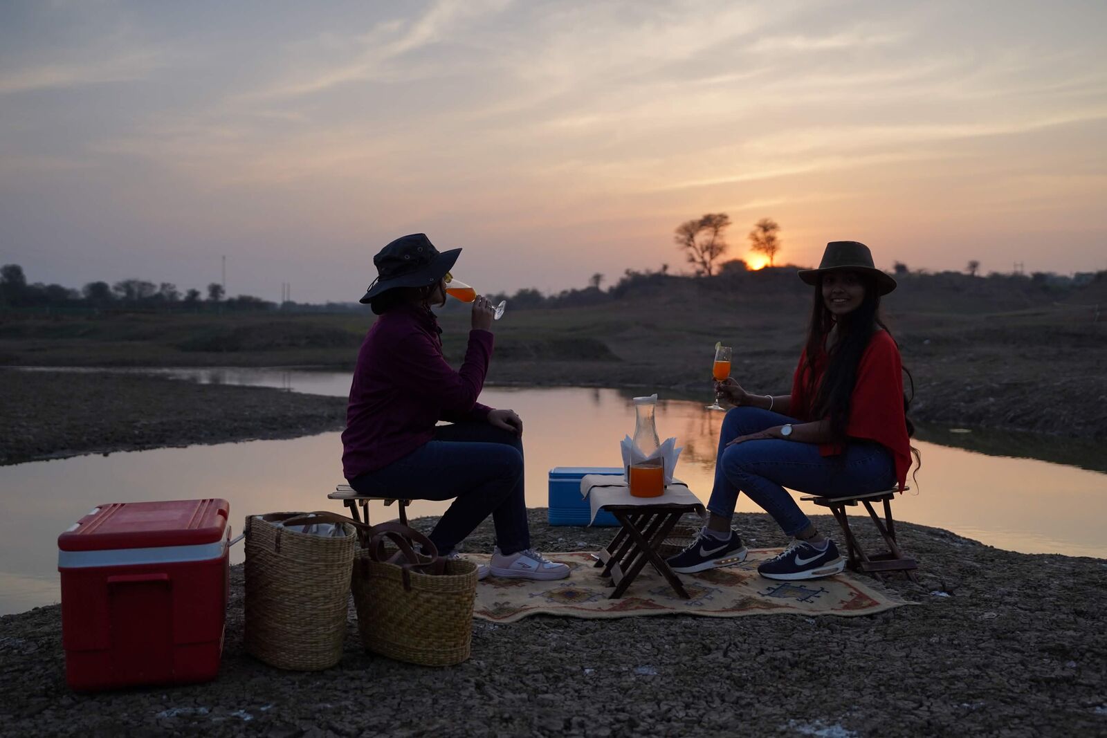 Two women sharing drinks at a lakeside sunset picnic