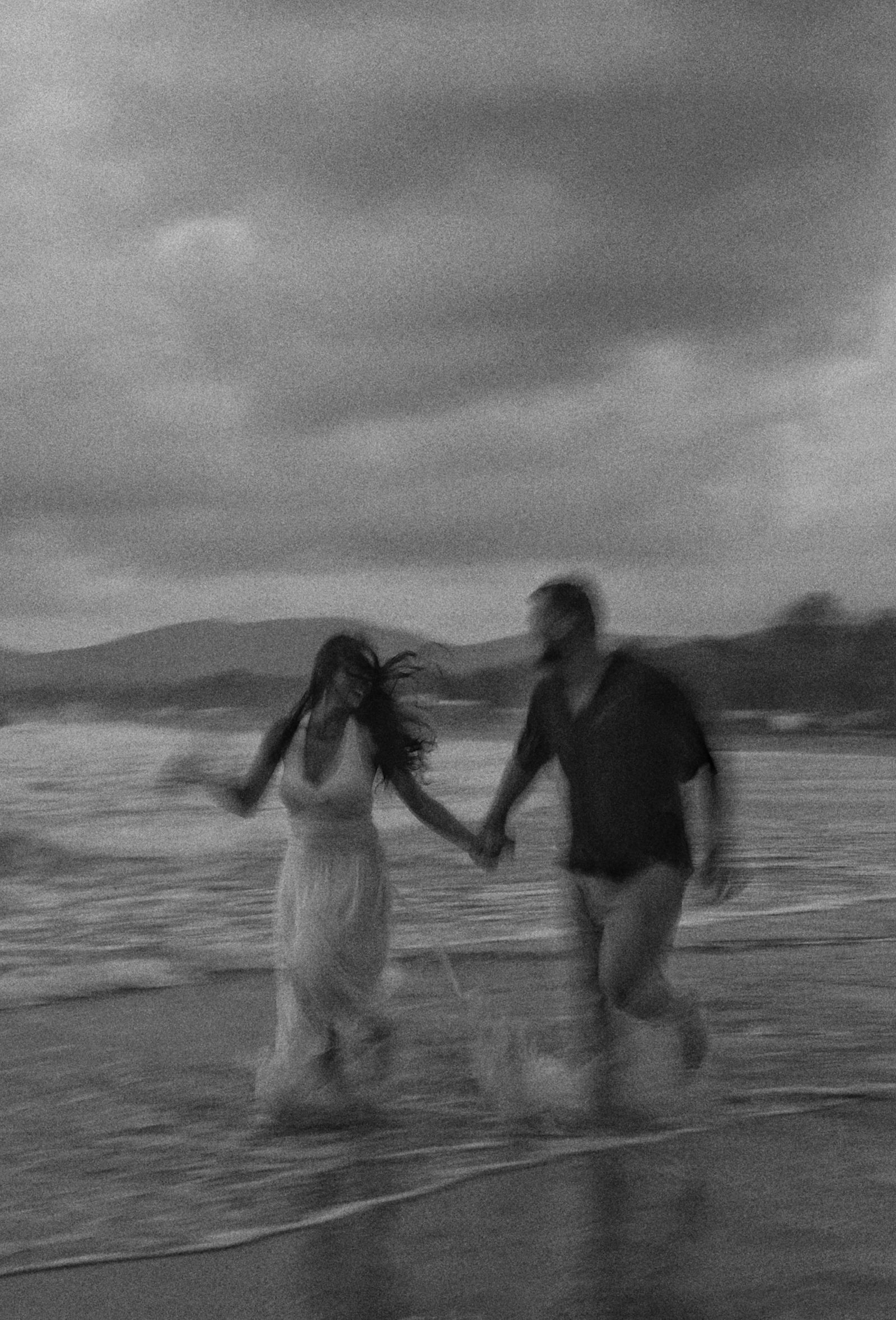 Couple walking hand in hand through the surf, black and white